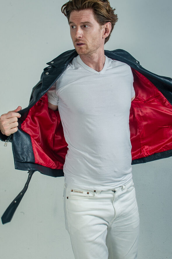 Portrait of a redhaired man wearing a black leather jacket, a white t-shirt and white jeans